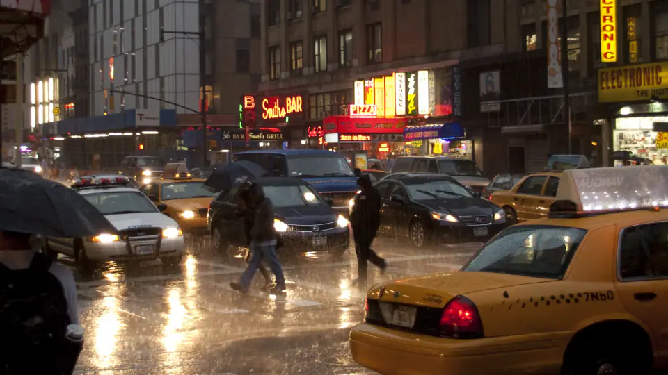 Pedestrians and cars on a rain-soaked Manhattan street at dusk.